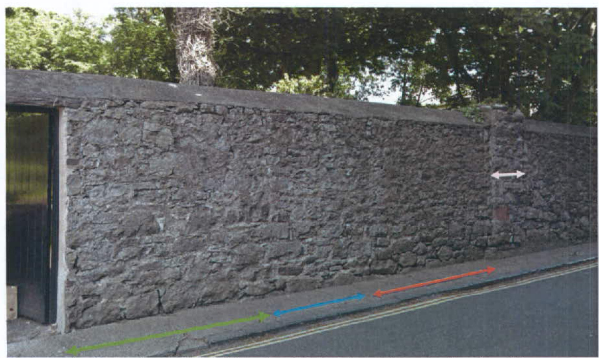 A photograph showing a long stone boundary wall along a roadside with colored arrows overlaid, likely indicating measurements or the proposed access location.