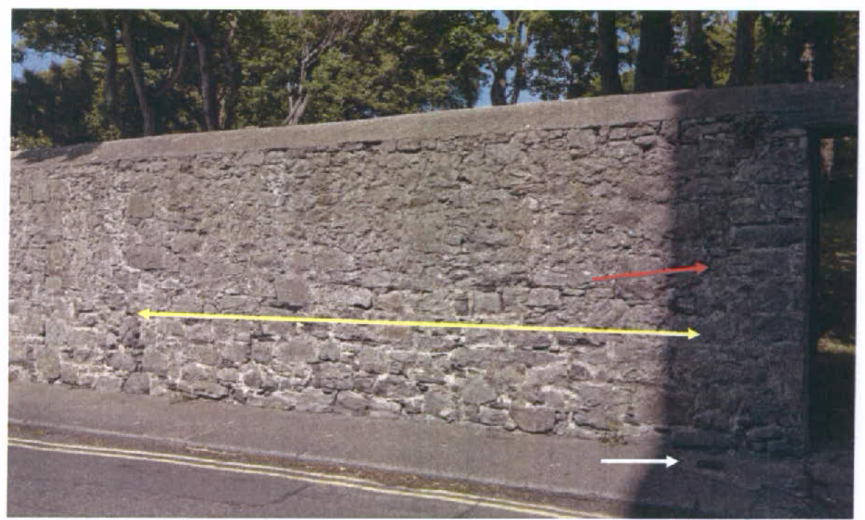 A photograph showing a long stone boundary wall along a road with overlaid yellow and red arrows indicating measurements or features.