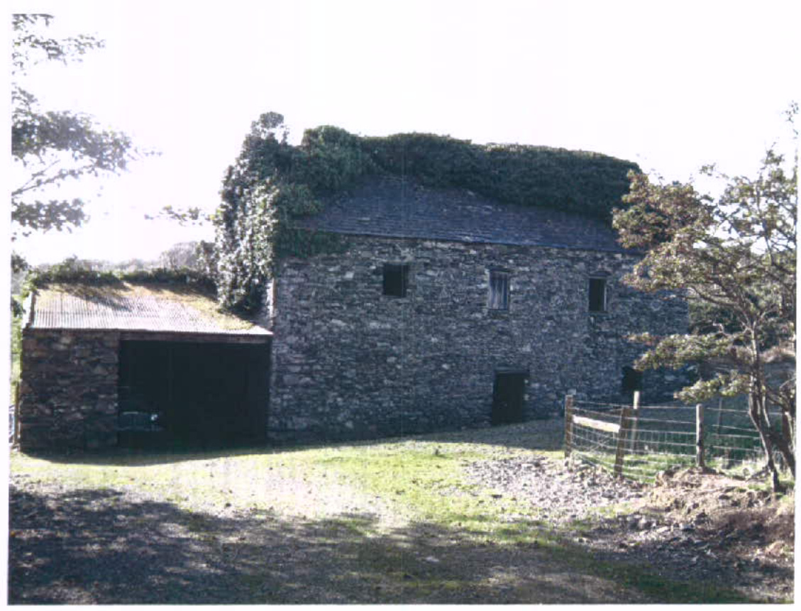 A photograph of a two-story stone building, likely a former mill or barn, with ivy growing on the roof and an attached single-story outbuilding.