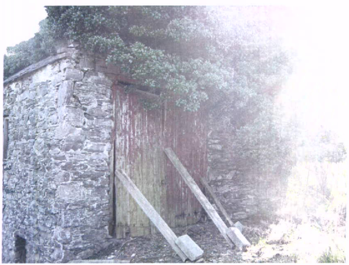 A photograph of an old stone building with large wooden doors and vegetation growing on the roof, likely the redundant mill mentioned in the application.