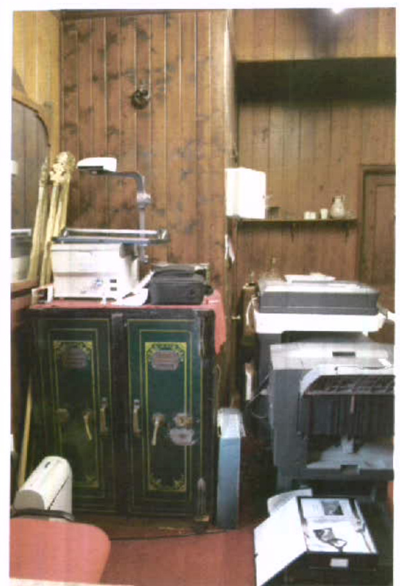 A photograph of an interior room with wood-paneled walls containing various pieces of equipment, including a green cabinet with gold detailing and white machinery.