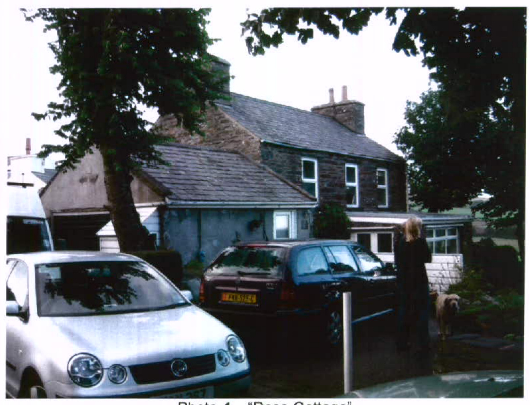 A photograph of a stone cottage named 'Rose Cottage' with cars parked in the driveway and a person standing nearby.