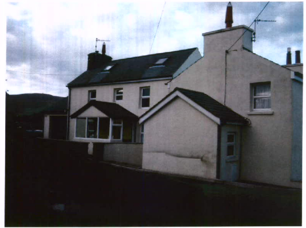 A photograph of a white, two-story detached house featuring a conservatory and a smaller single-story outbuilding or garage attached to the front.