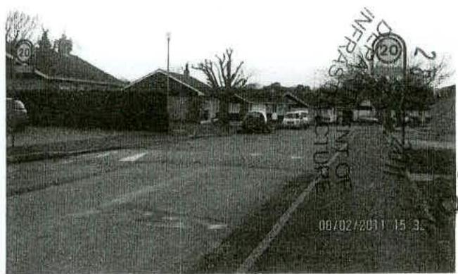 Grainy black and white photograph of a street scene showing single-story buildings, likely the existing dental surgery, with a road and speed limit sign in the foreground.