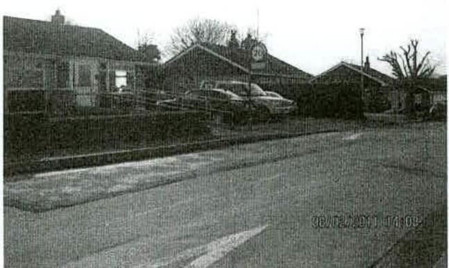A grainy black and white photograph showing the exterior of a commercial building complex with parked cars and a road in the foreground.