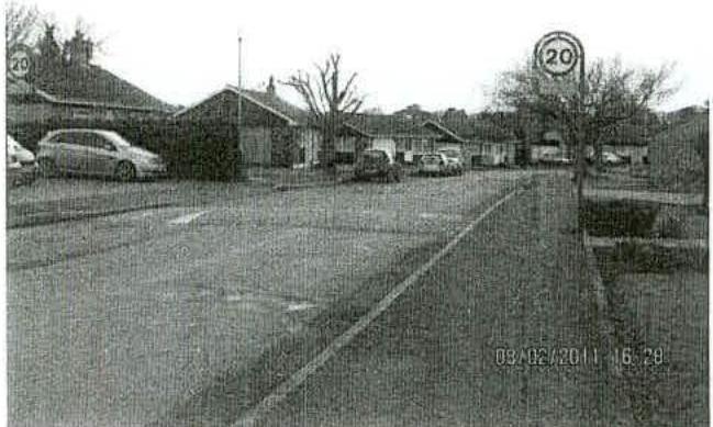 A grainy black and white photograph showing a street scene with parked cars and single-story buildings, likely the existing dental surgery site.
