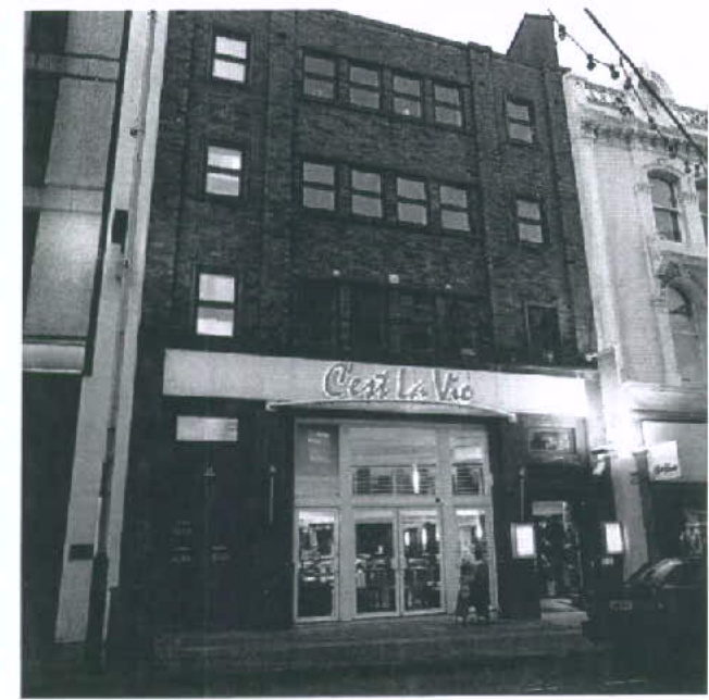 A black and white photograph showing the street-facing facade of a multi-story commercial building with a shop front.