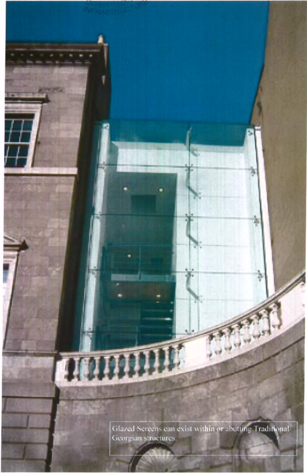 A photograph showing a modern multi-story glass extension attached to a traditional stone building with a balustrade in the foreground.