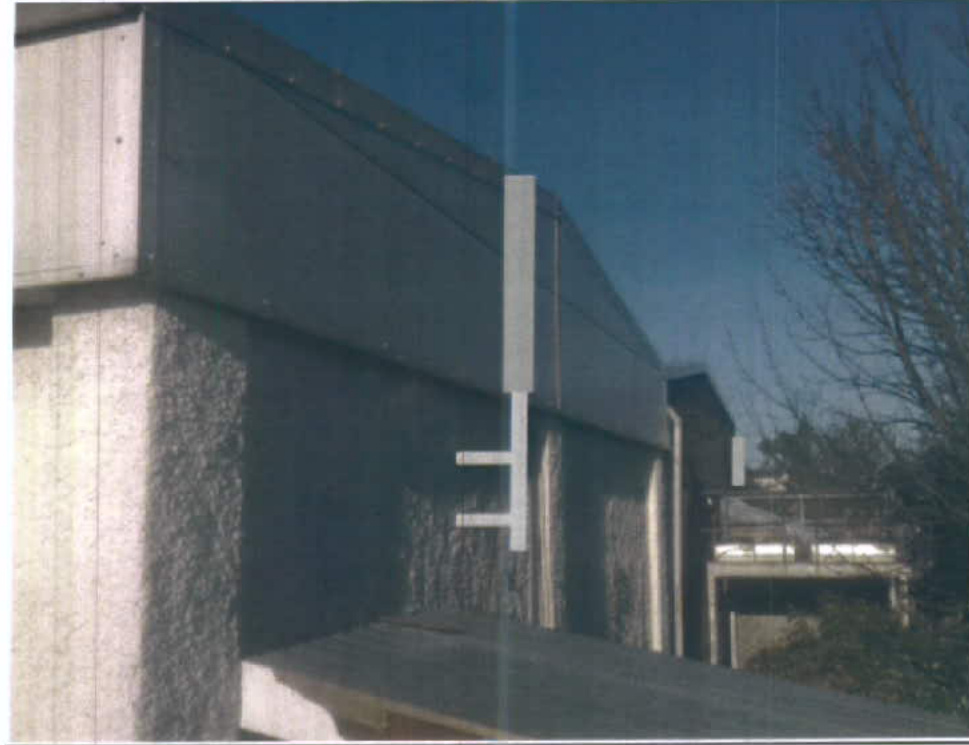 A photograph showing the side elevation of a concrete building with white mounting brackets attached to the wall, likely for the proposed telecommunications antennas.
