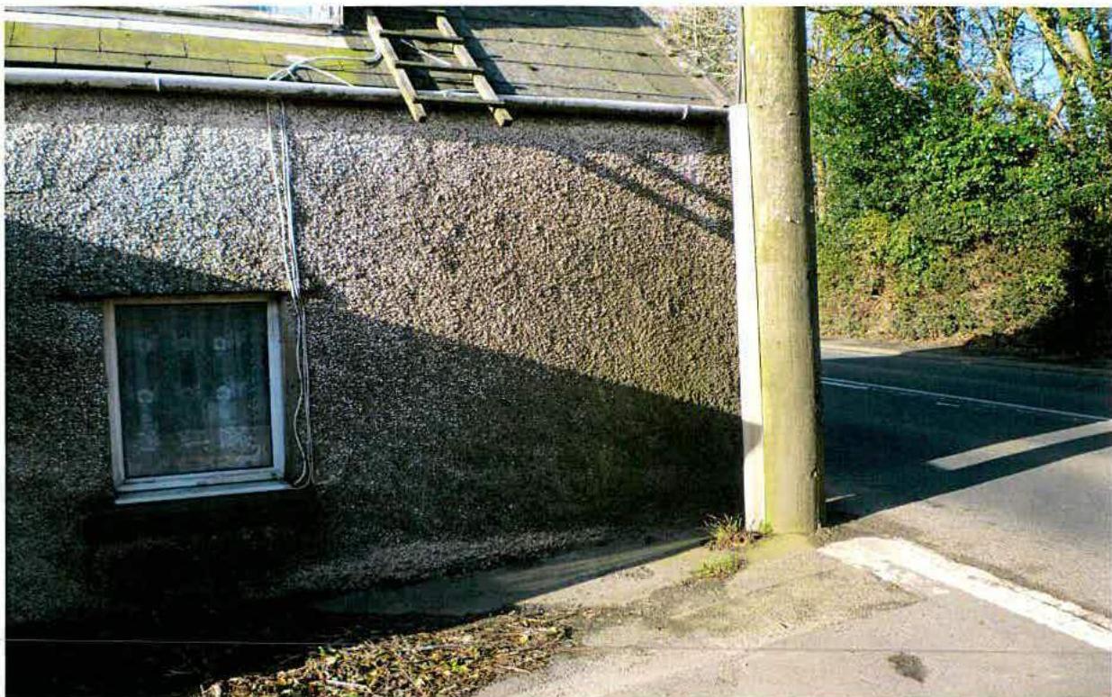 A photograph showing the side of a pebbledash building with a window and a ladder, situated next to a road and a utility pole.