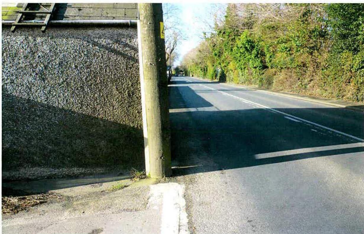 A photograph showing a rural road junction with a textured wall and wooden utility pole on the left side.