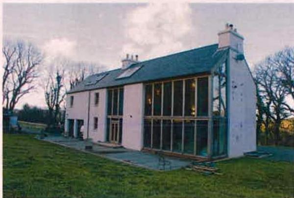 A photograph showing a white detached building, likely a listed property, featuring a large modern two-story glass extension attached to the side.