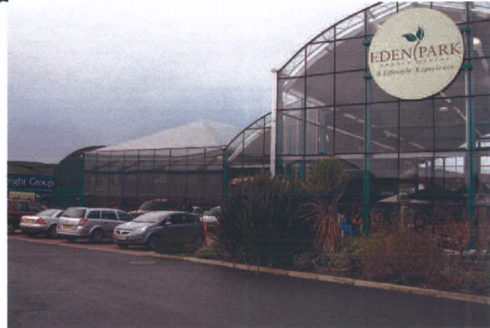 A photograph showing the exterior of a large commercial glass building with a sign reading 'Eden Park' and cars parked in the foreground.