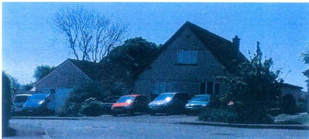 A grainy, blue-tinted photograph showing a detached house with a pitched roof and an attached structure to the left, with several cars parked in the driveway.
