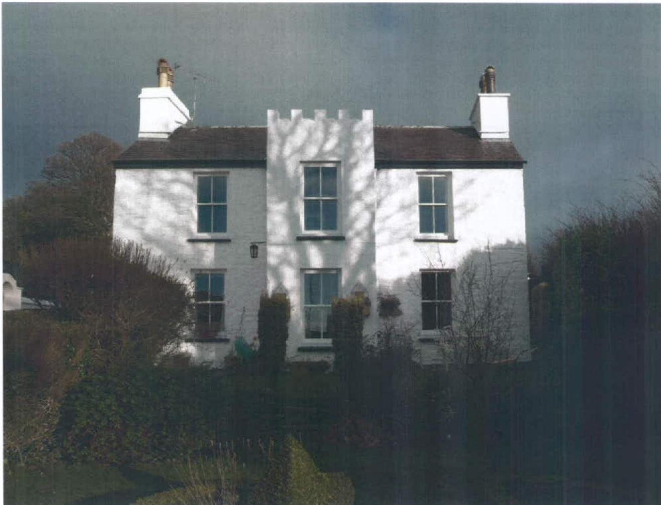 A photograph of a white, two-story house featuring crenellated detailing on the central bay and prominent chimneys.