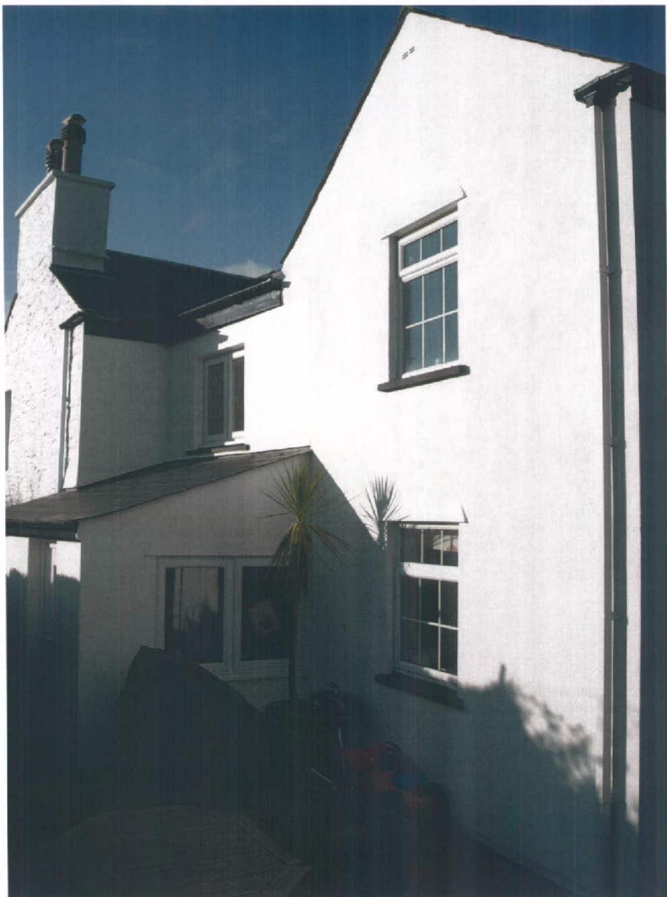 A photograph showing the side elevation of a white two-story residential building with a single-story extension attached to the left.