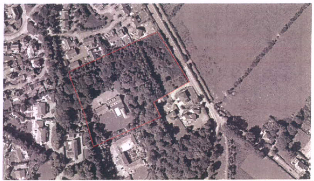 An aerial view showing the application site outlined in red, featuring a large wooded area adjacent to a road and nearby houses.