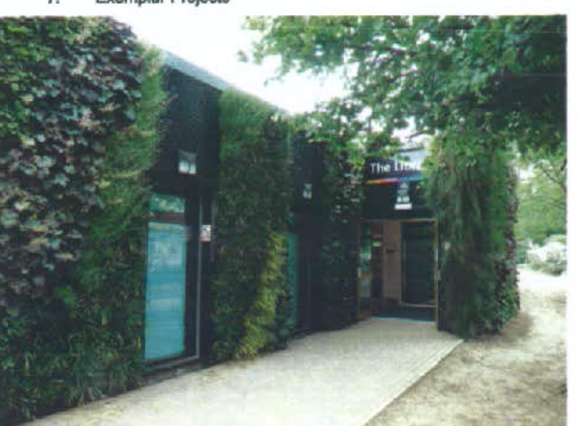 A photograph of a modern building featuring a living wall facade covered in greenery and a paved walkway leading to an entrance.