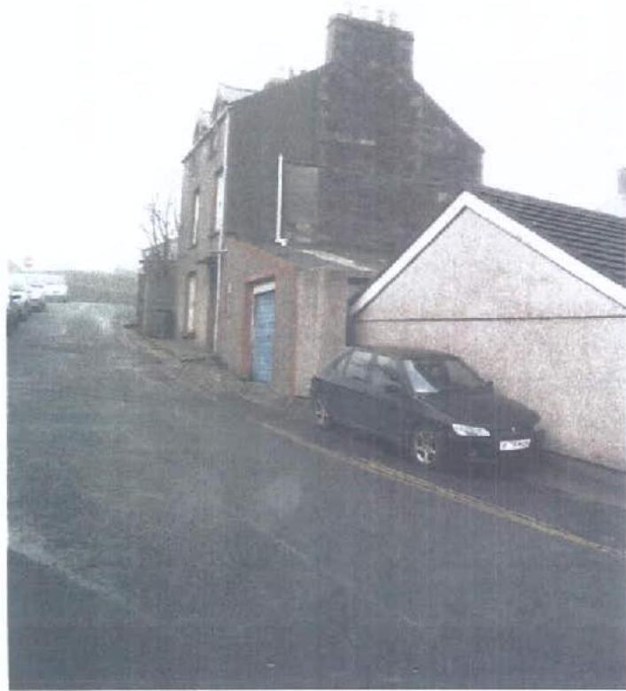 A grainy street-level photograph showing a two-story building with a blue garage door and an adjacent lower white-walled structure with a car parked in front.