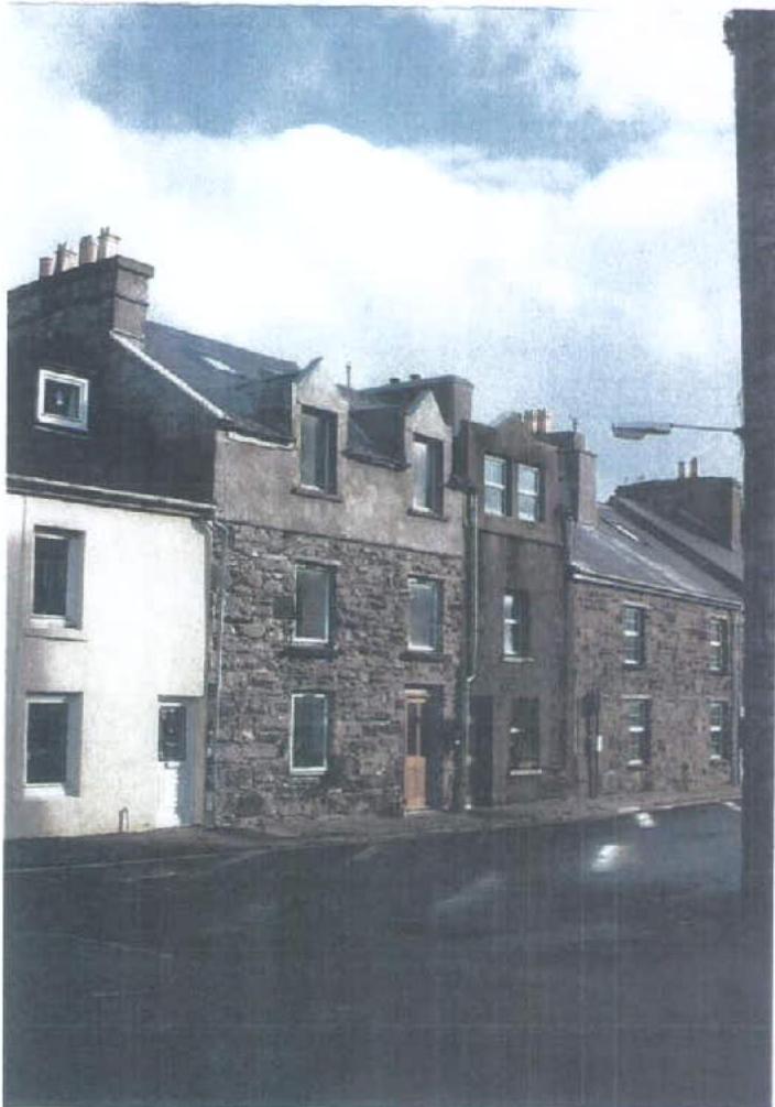 A grainy photograph showing a row of traditional stone and rendered terraced buildings with dormer windows and chimneys under a cloudy sky.