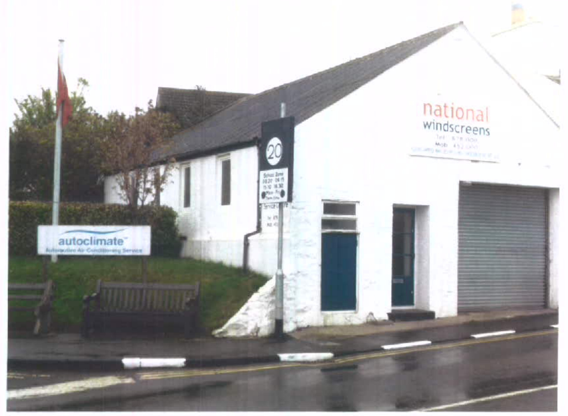 A street-level photograph of a white commercial building featuring a roller shutter door and 'national windscreens' signage, with a separate 'autoclimate' sign on a post in the foreground.