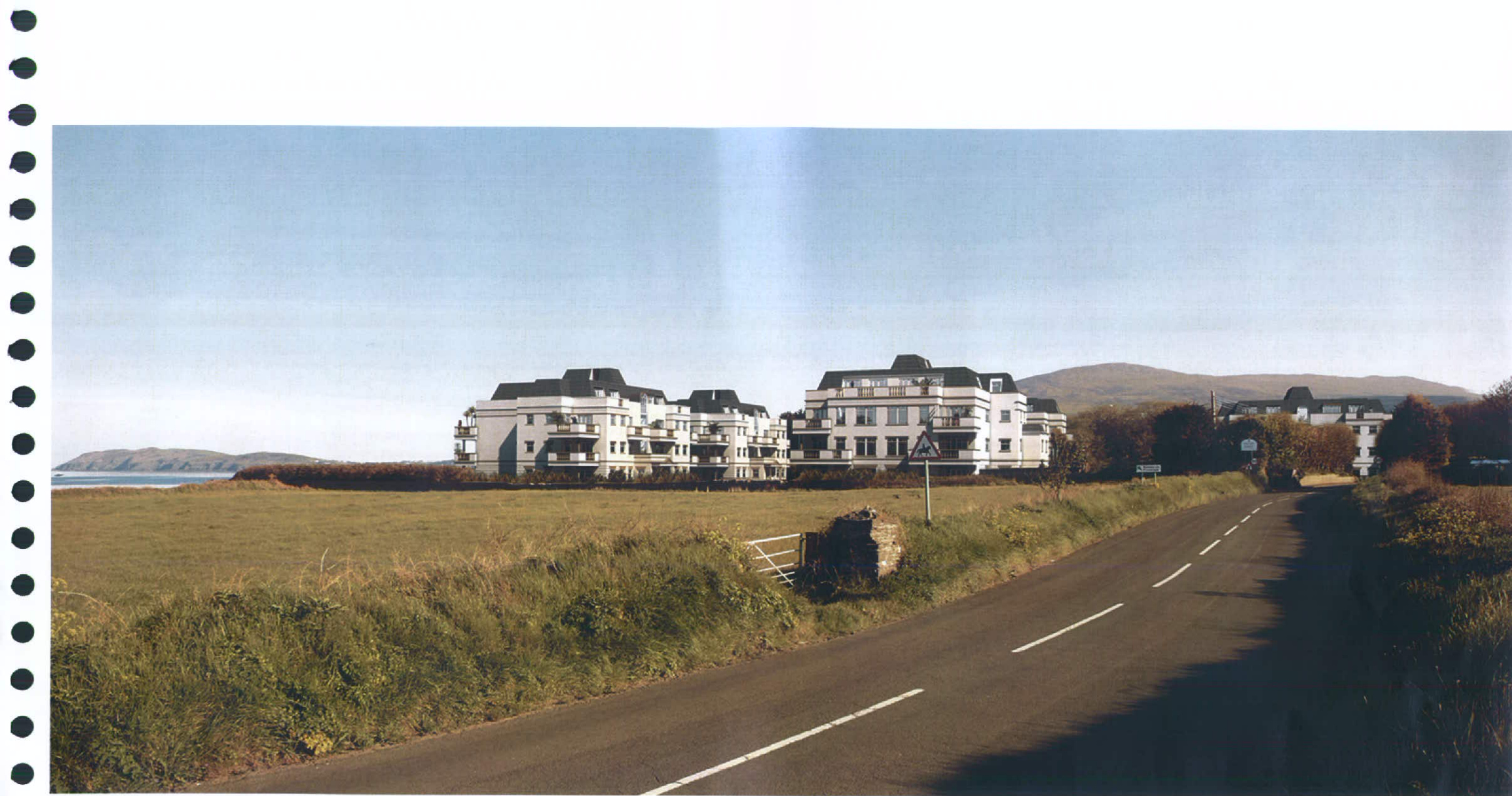 A perspective view or photomontage showing a large white multi-story apartment complex situated next to a road and coastal landscape.
