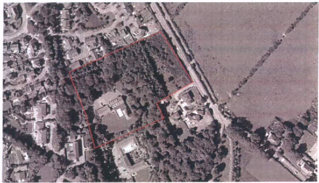 An aerial view showing a plot of land outlined in red, situated between a residential area and open fields.