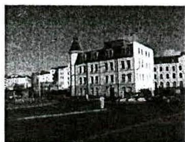 A grainy black and white photograph showing a large multi-story building with a tower feature.