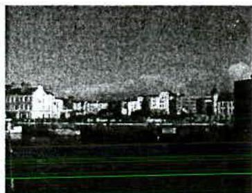 A grainy, low-quality photograph showing a row of multi-story buildings along a waterfront or street.