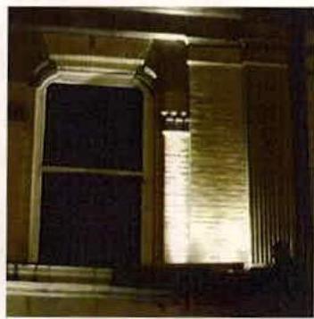 A night-time photograph showing a building facade with a large sash window and illuminated stonework.
