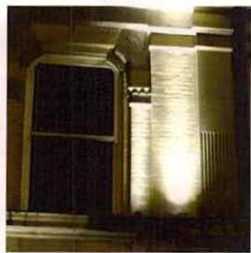 A night-time photograph showing the exterior of a building with a window and brick wall illuminated by external uplighting.