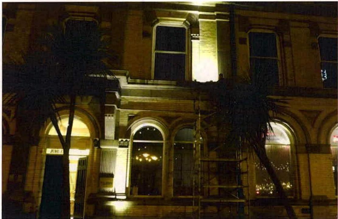 A night-time photograph showing the illuminated exterior facade of a building with arched windows and scaffolding.