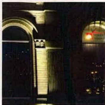 A night-time photograph showing the illuminated facade of a stone building with arched windows and columns.