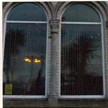 A close-up photograph of a building facade featuring two large arched windows separated by a stone column, taken at night.
