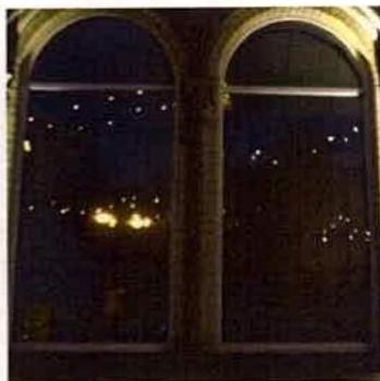 A grainy night photograph showing two large arched windows with lights visible in the background or reflections.
