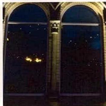A grainy night-time photograph showing a stone building facade with two large arched openings, likely illustrating the effect of external lighting.