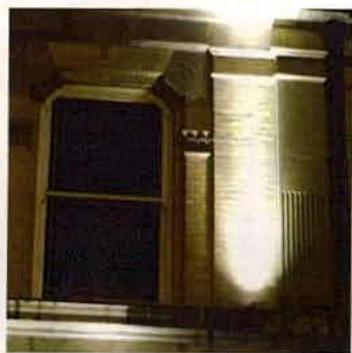 A night-time photograph showing a close-up of a stone building facade with a window and a beam of external light illuminating the wall.