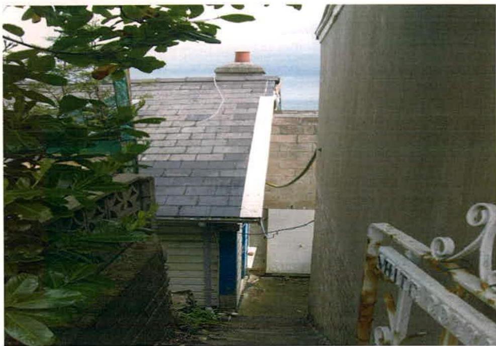 A photograph showing a narrow passage between buildings with a slate roof and a view of the sea in the background.