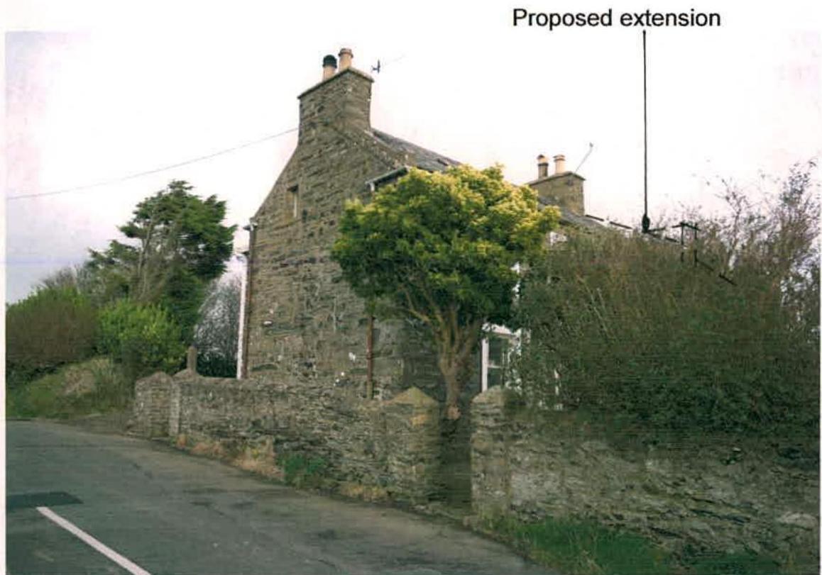 A photograph of a stone dwelling with a stone wall and road in the foreground, annotated with a line indicating the location of a proposed extension.