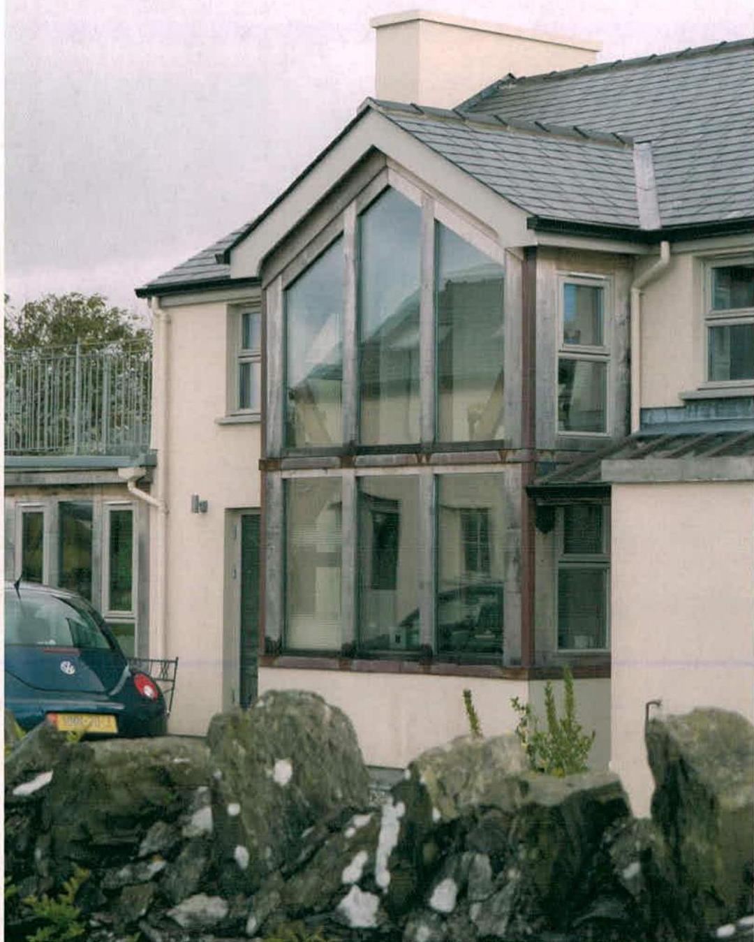 A photograph of a detached house featuring a prominent two-storey glass extension with a stone wall in the foreground.