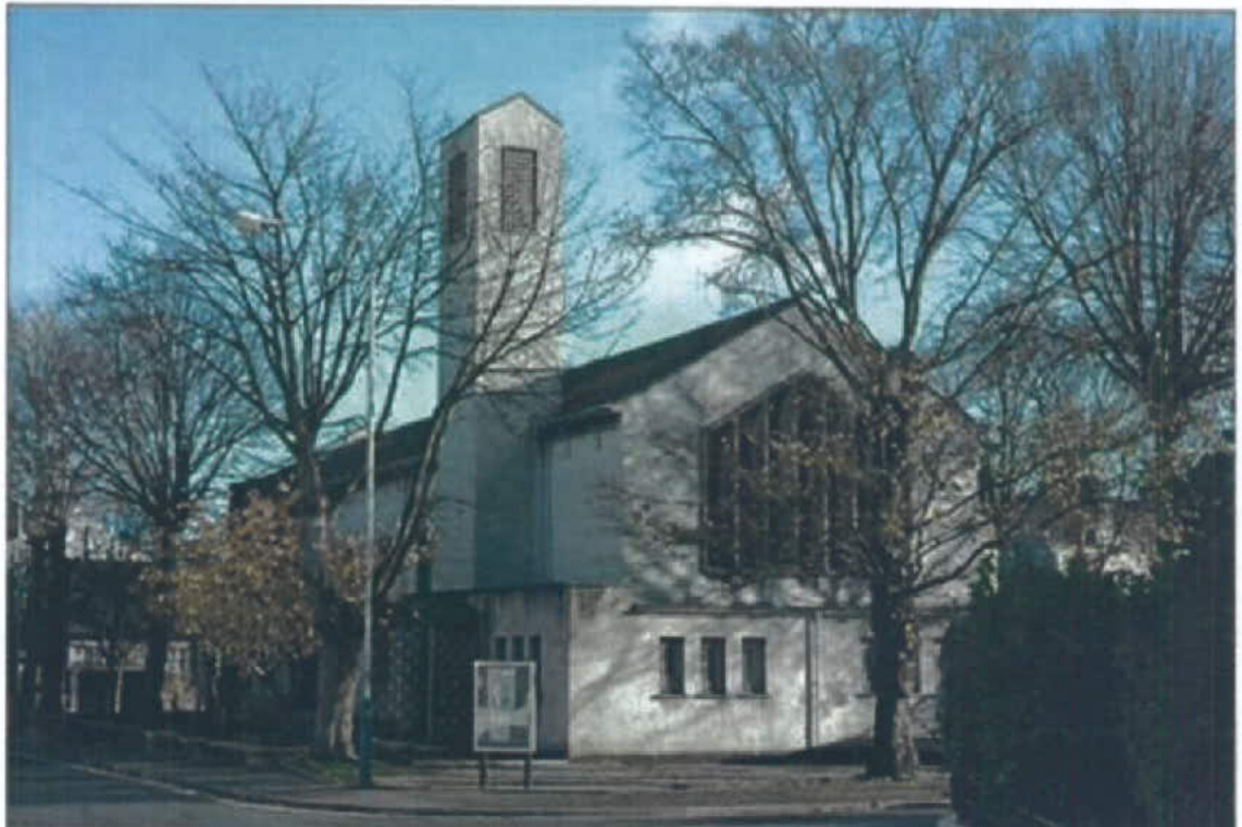 A photograph showing the exterior of a white, modernist-style building with a prominent bell tower, likely a church, surrounded by bare trees.