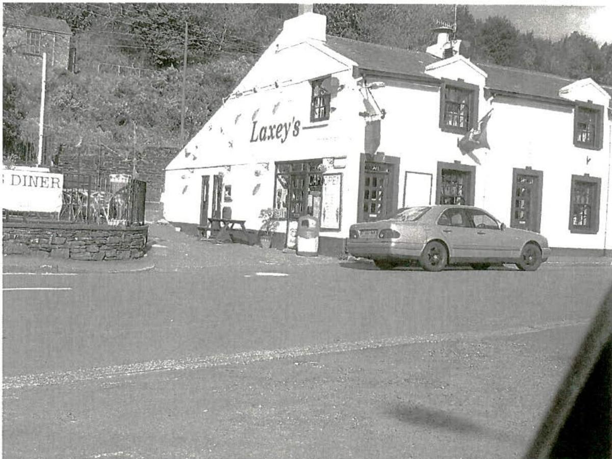 A black and white photograph showing the exterior of a white building labeled 'Laxey's' with a car parked in the foreground paved area.