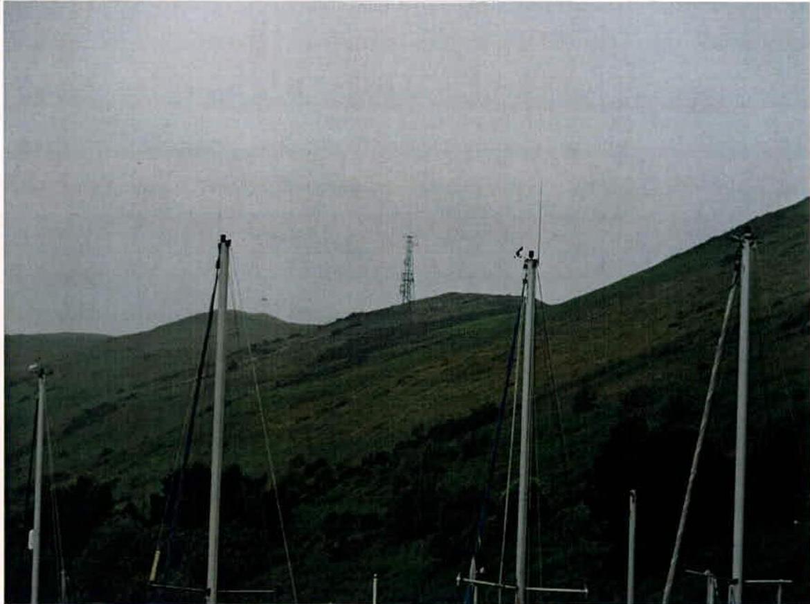 A grainy photograph showing a grassy hill with a lattice communication tower in the distance and tall masts in the foreground.