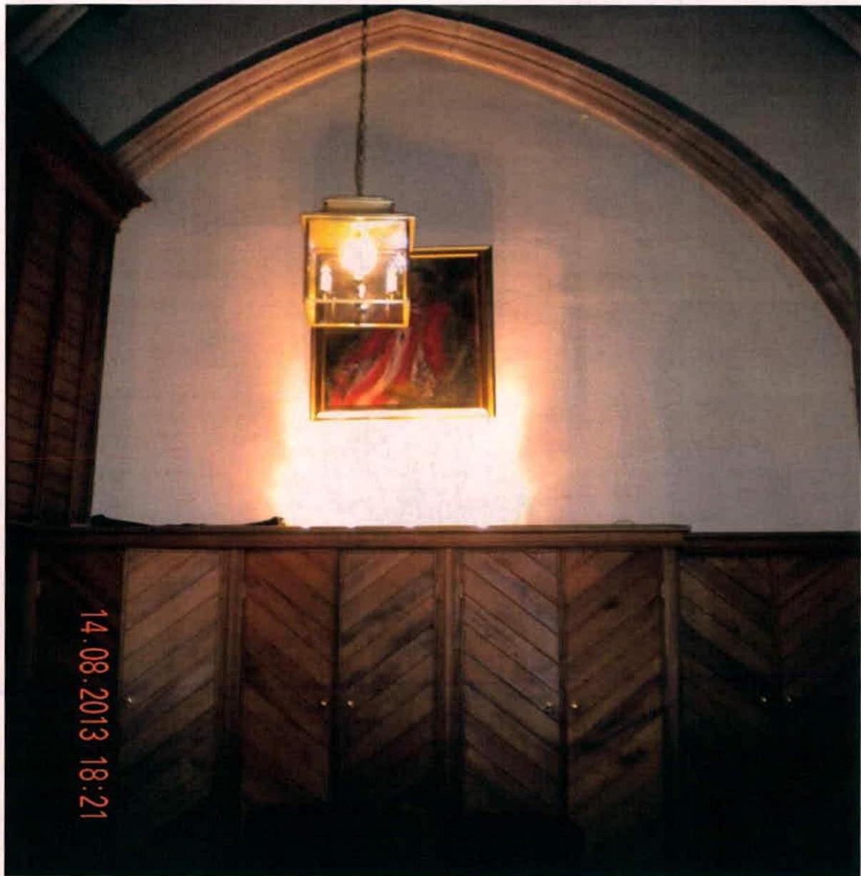 An interior photograph showing a wall with wooden chevron paneling and a large archway, illuminated by a hanging light fixture.