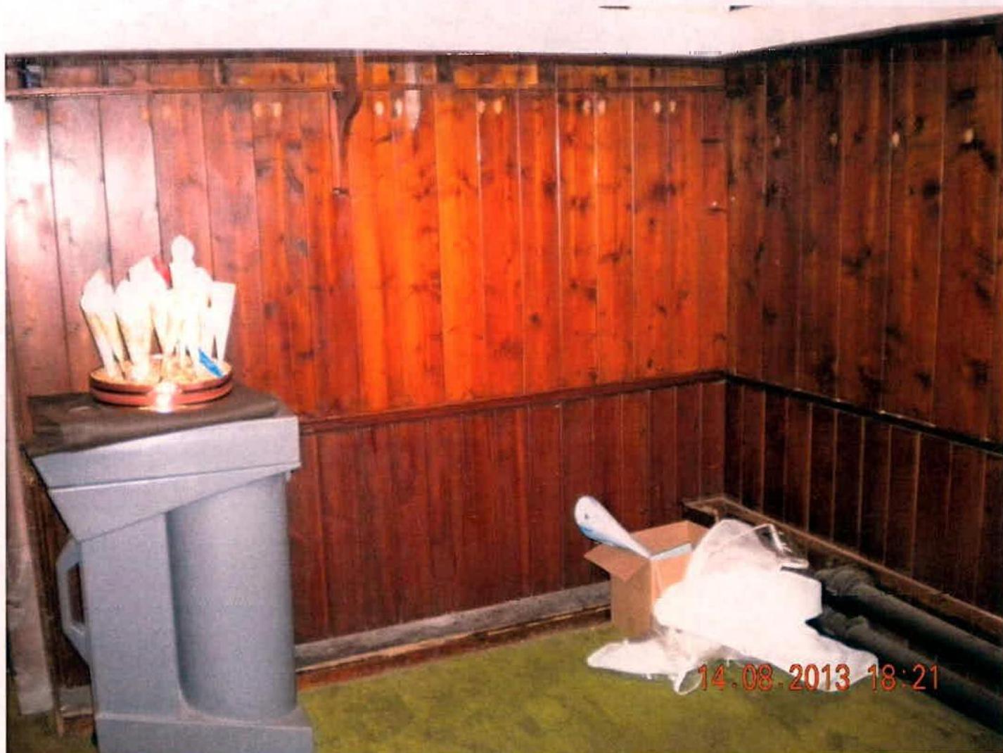A photograph of an interior room with wood paneling, featuring a grey lectern and construction materials on the floor.