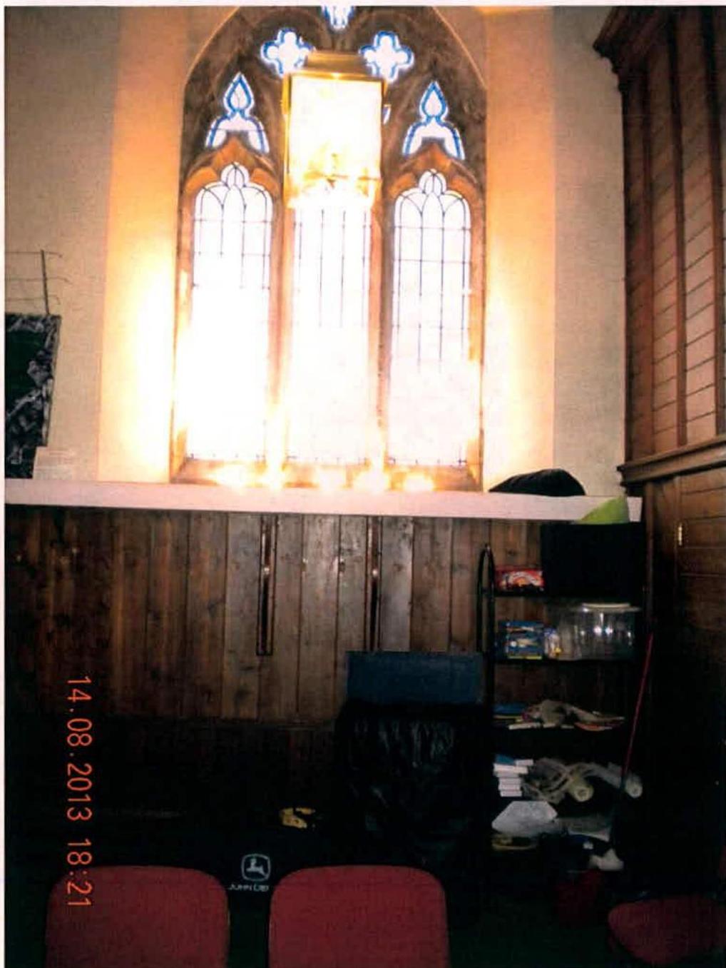 Interior photograph of a room featuring a large arched window with leaded glass and wooden paneling.
