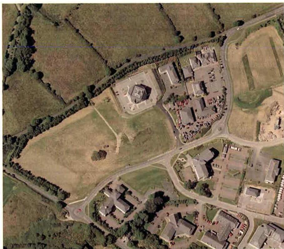 An aerial view of a rural site showing a proposed development area with adjacent buildings and parking lots.