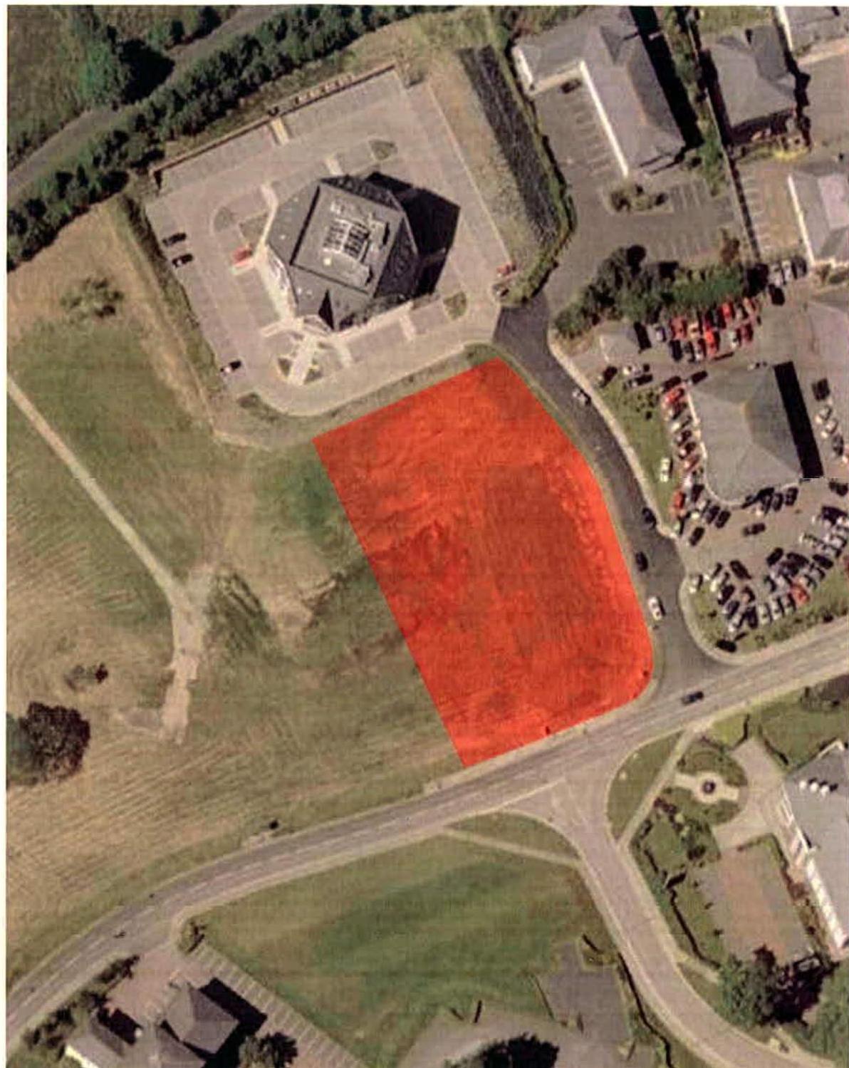 Aerial view site plan showing a plot of land highlighted in red, located adjacent to an existing commercial building and road.