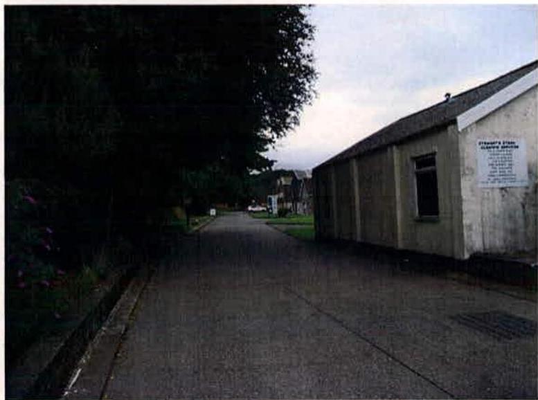 A photograph showing a paved path running alongside a single-story building with a sign on the wall, likely the subject of the demolition consent.