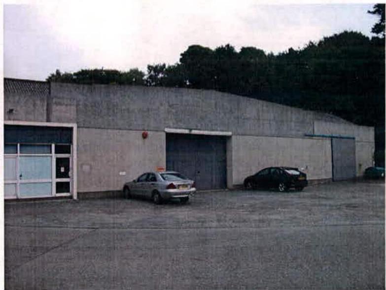 A photograph showing the exterior of a large, single-story concrete building with multiple garage-style doors and cars parked in front.